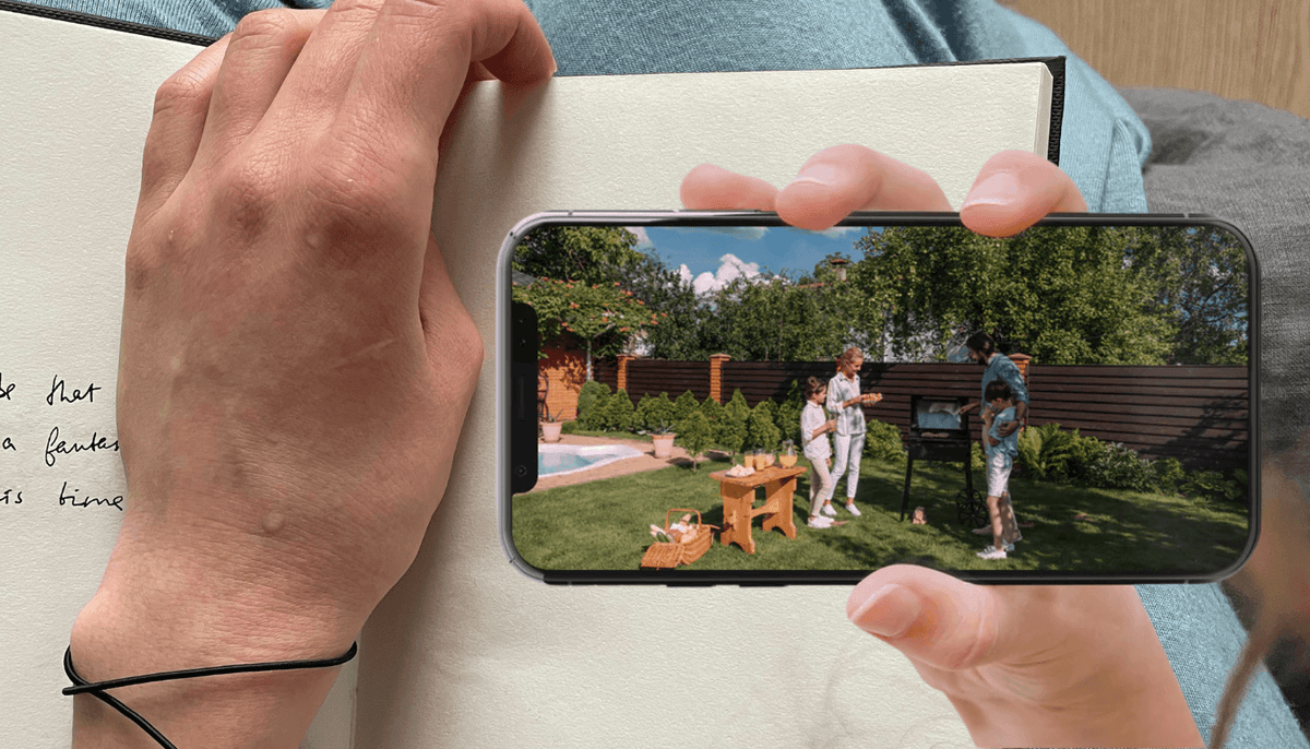 Person viewing a Toucan S4 camera feed on a smartphone beside a notebook