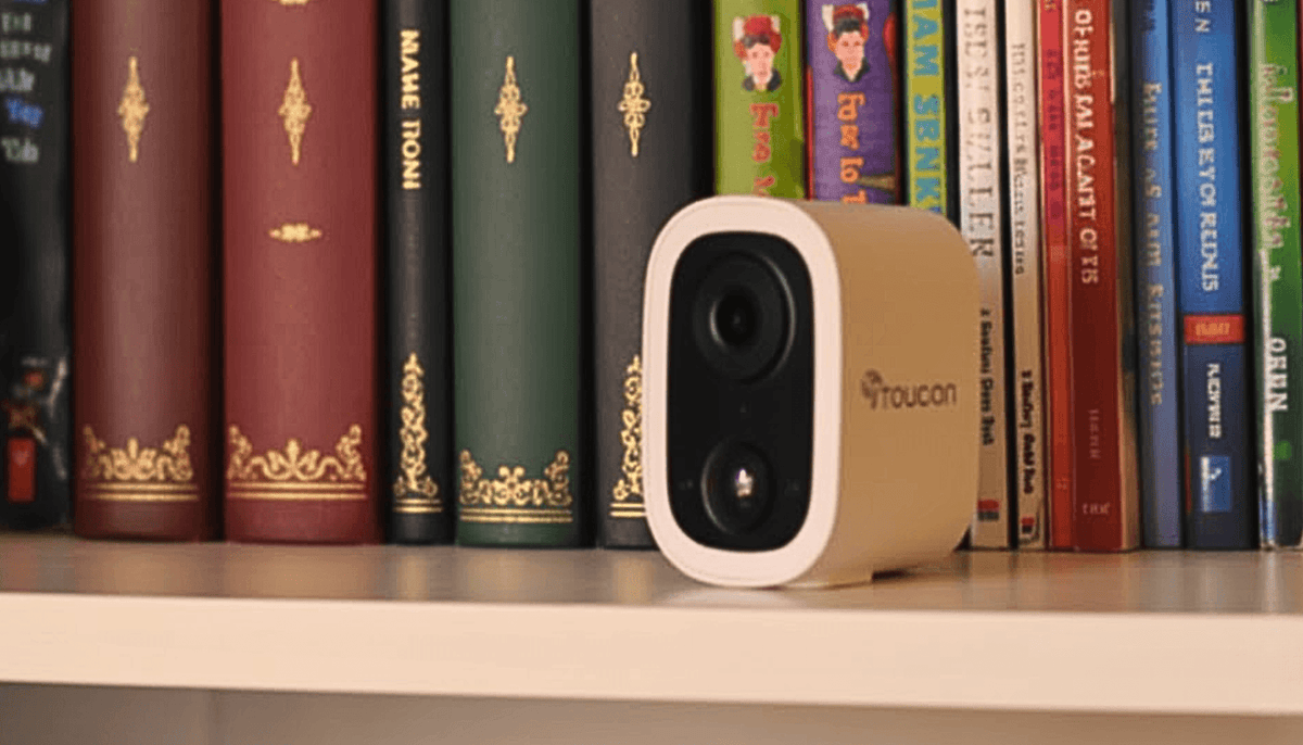 Toucan S4 wireless security camera on a shelf beside books