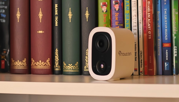 Toucan Solutions S4 wireless home security camera on a shelf with old books