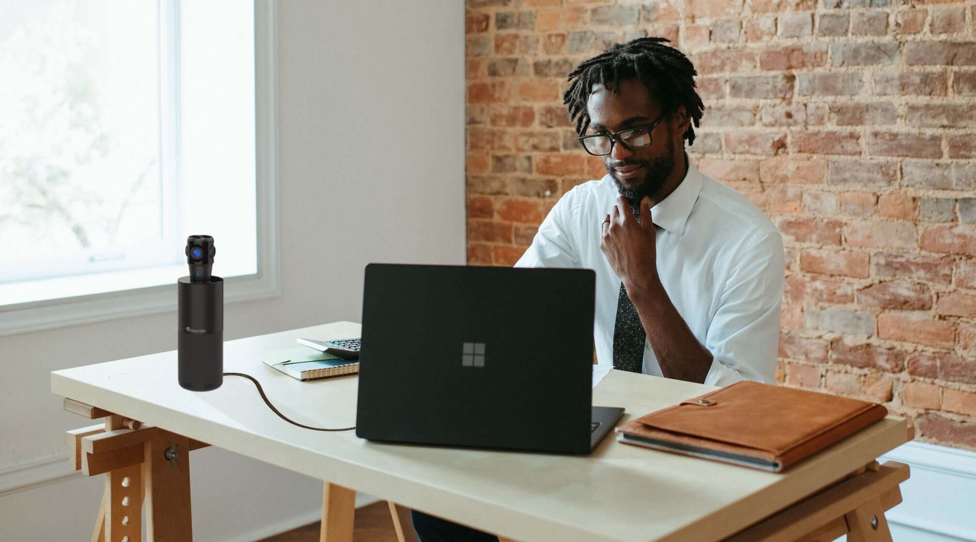 Why Small Businesses Need 360 Conference Cameras | small business owner sitting in front of laptop with the Toucan Video Conference System 360 on the table