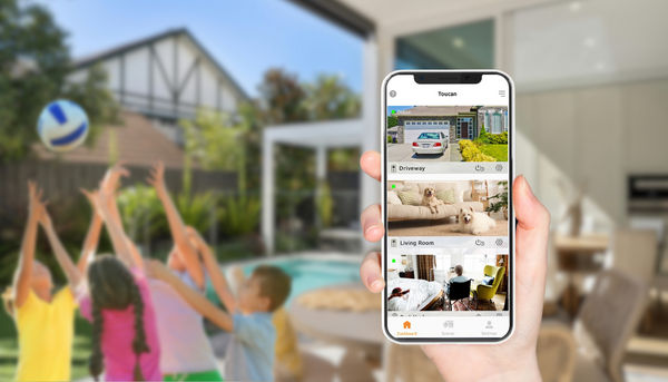hand holding up smartphone camera showing real time feed of the toucan solutions s4 with a background of a yard with swimming pool and kids playing ball